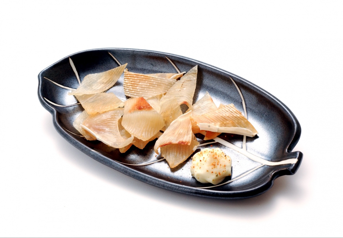 Blue ceramic leaf-shaped plate filled with dried bonito flakes and a small dollop of mayonnaise with chili flakes on the side.