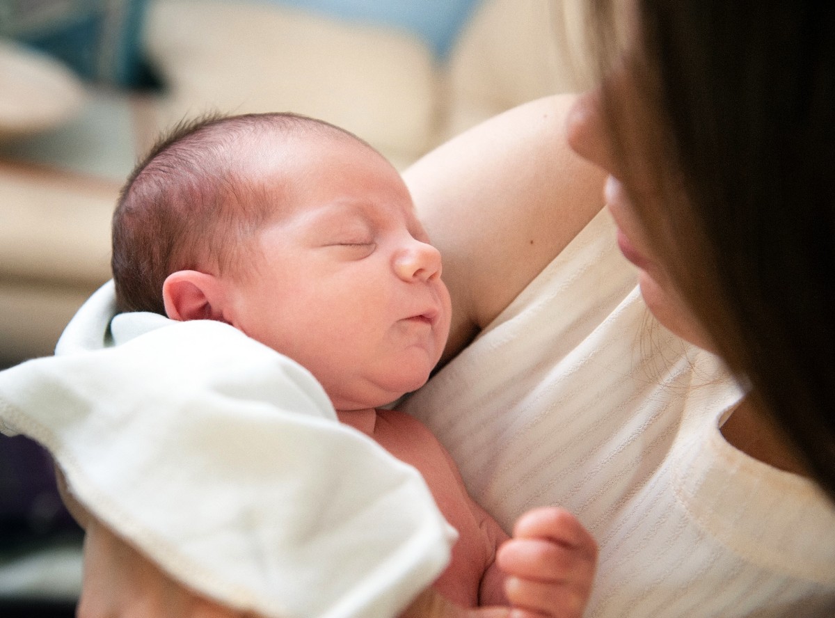 Sleeping newborn cradled in a caregiver's arms, close-up profile view of the baby and gentle embrace of the parent