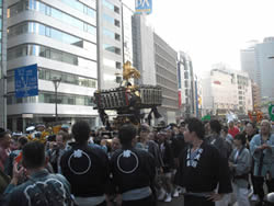 私たちの「ふるさと創り」に一役買った貴重な思い出、山王祭。赤阪見附のビルを背にお神輿を担ぎ、永田町へと歩を進める人たち。