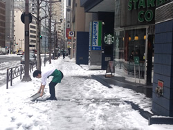 東京が大雪に見舞われた週末、店の前で雪かきをするスターバックス店員。