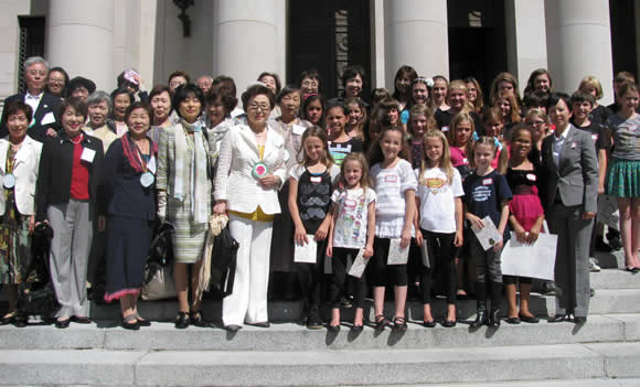 naoko-sokolik-4 - junglecity.com Large diverse group of adults and children posing on building steps for a group photo, many with name badges and folders in hand.