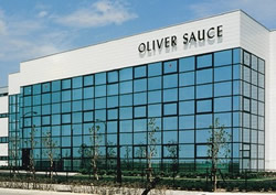 Modern office building with blue glass windows and 'Oliver Sauce' sign across the top exterior.