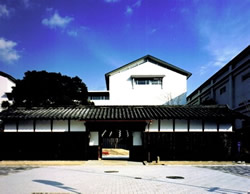 Front view of a traditional Japanese-style building with white upper floors and dark wooden lattice walls under a bright blue sky.