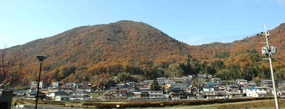 Small town at the base of a forested hill in autumn colors under a clear blue sky.
