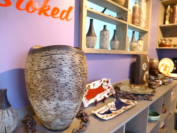 Large woven vase on a display shelf in a purple-walled pottery shop, with ceramic vases and bowls around it.