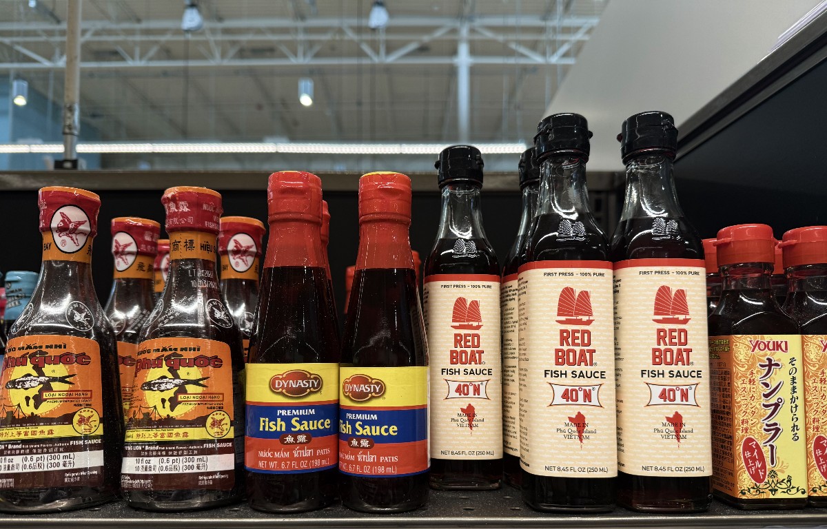 Assorted fish sauce bottles on a store shelf, including Dynasty and Red Boat brands with red caps and beige labels.