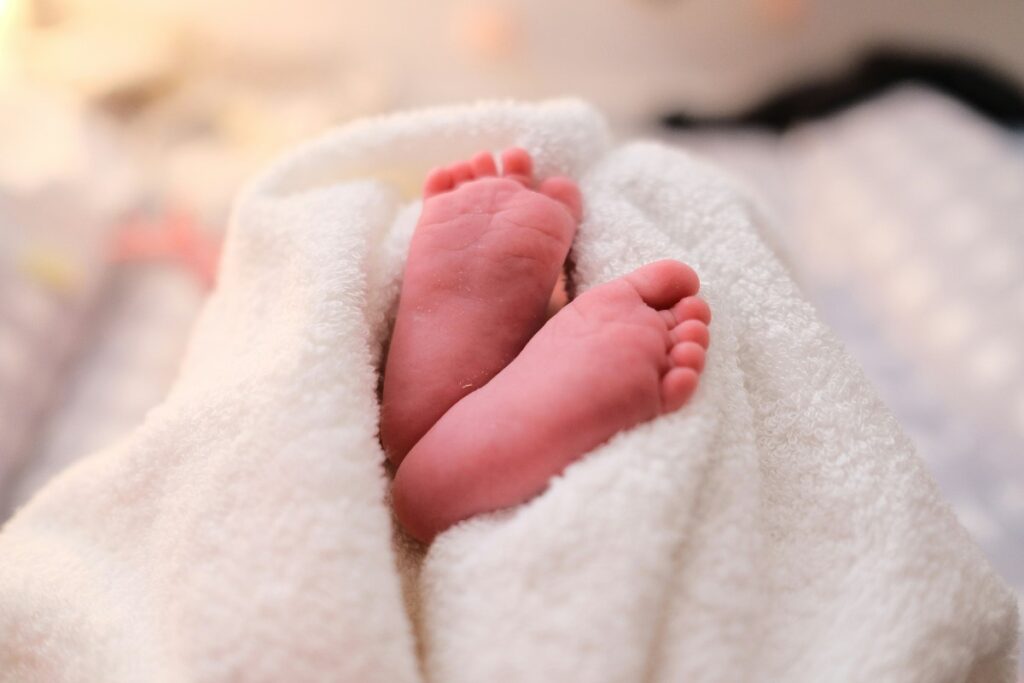 Tiny newborn feet poking out from a fluffy white towel, wrapped in a gentle scene.
