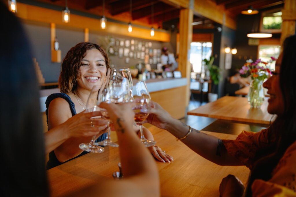 Group of friends toasting with wine glasses at a wooden bar, smiling and enjoying a casual gathering.