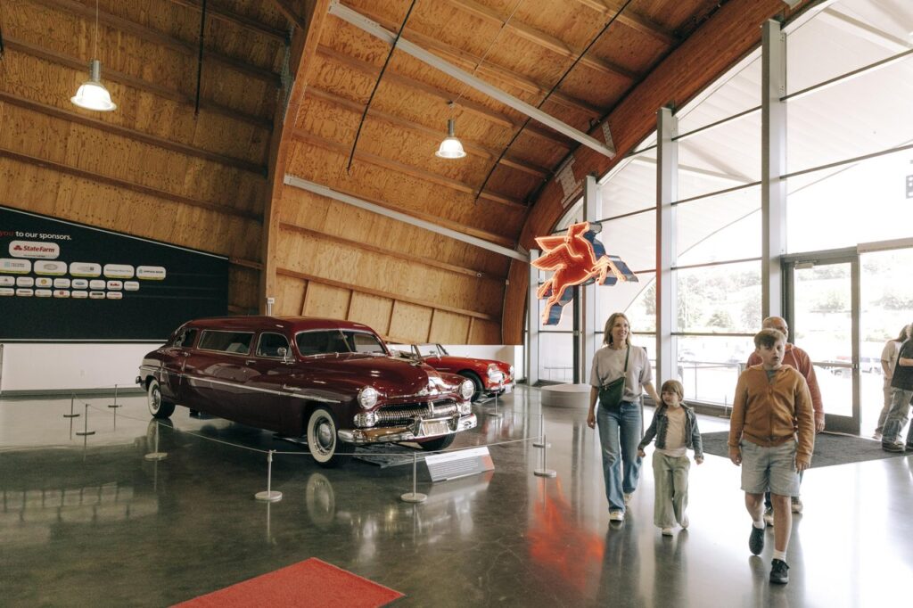 tacoma-lemay-2 - junglecity.com Family of four walks through an automotive museum with vintage cars on display and a neon horse sign nearby.