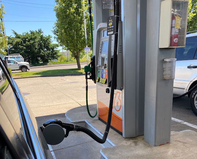 Gas pump at a sunny fueling station with a car connected and the nozzle in use?