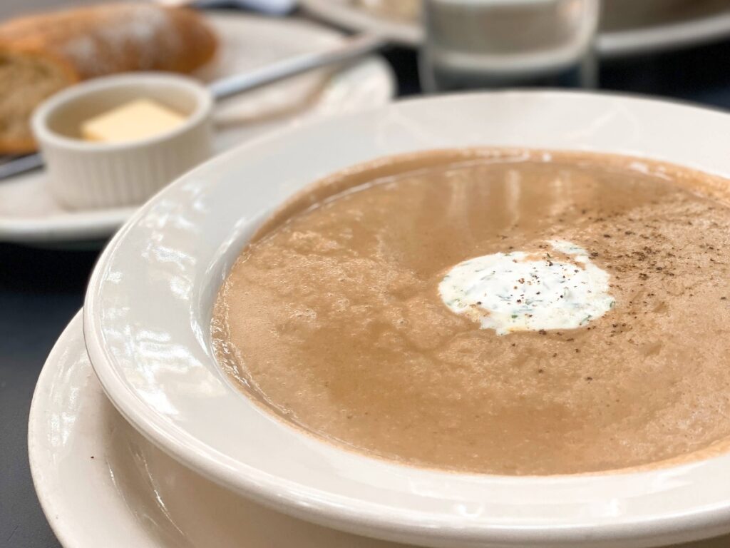 le-pichet-2 - junglecity.com Bowl of creamy soup with a dollop of sour cream and pepper on top, with bread and butter in the background.