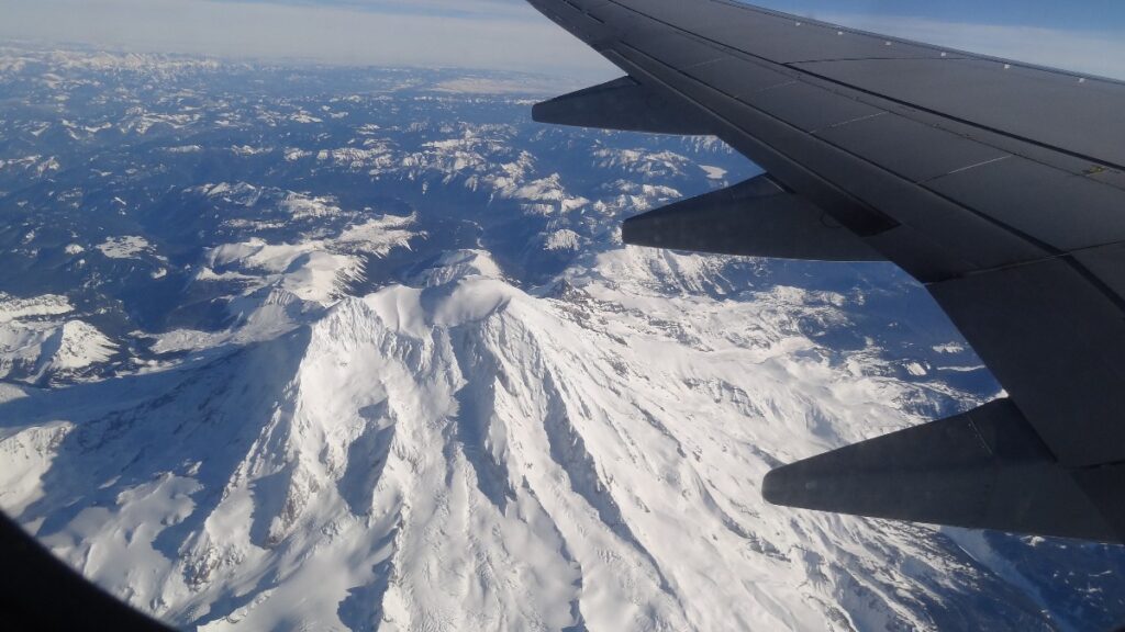 mount-rainier-65 - junglecity.com Snowy mountain range seen from an airplane window with the wing in the foreground.