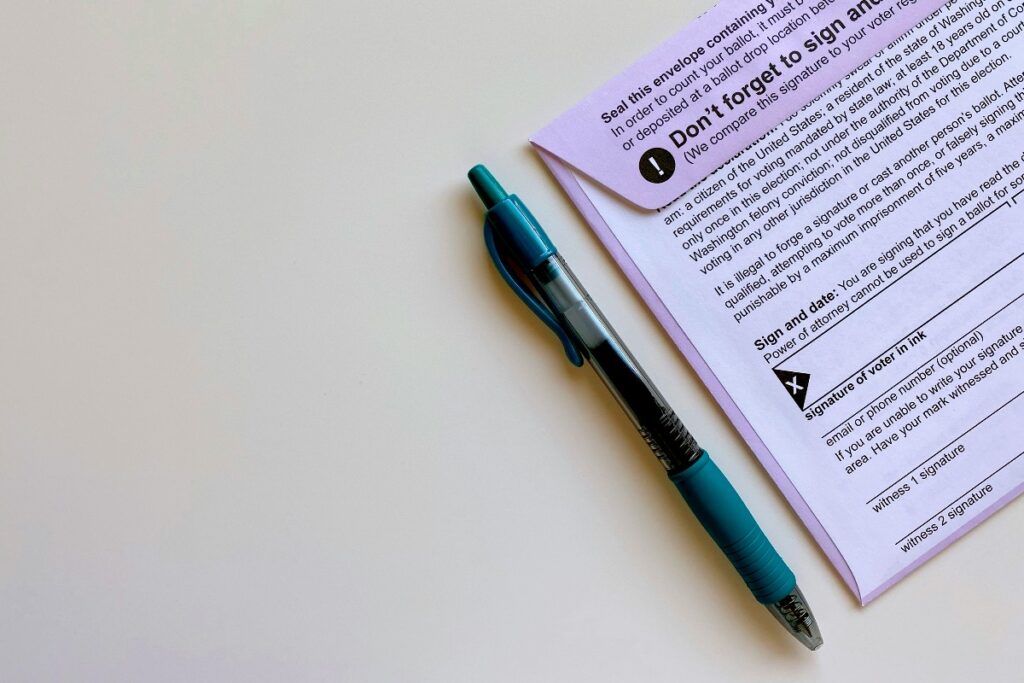 Blue and teal pen beside a purple voting ballot on a white surface.