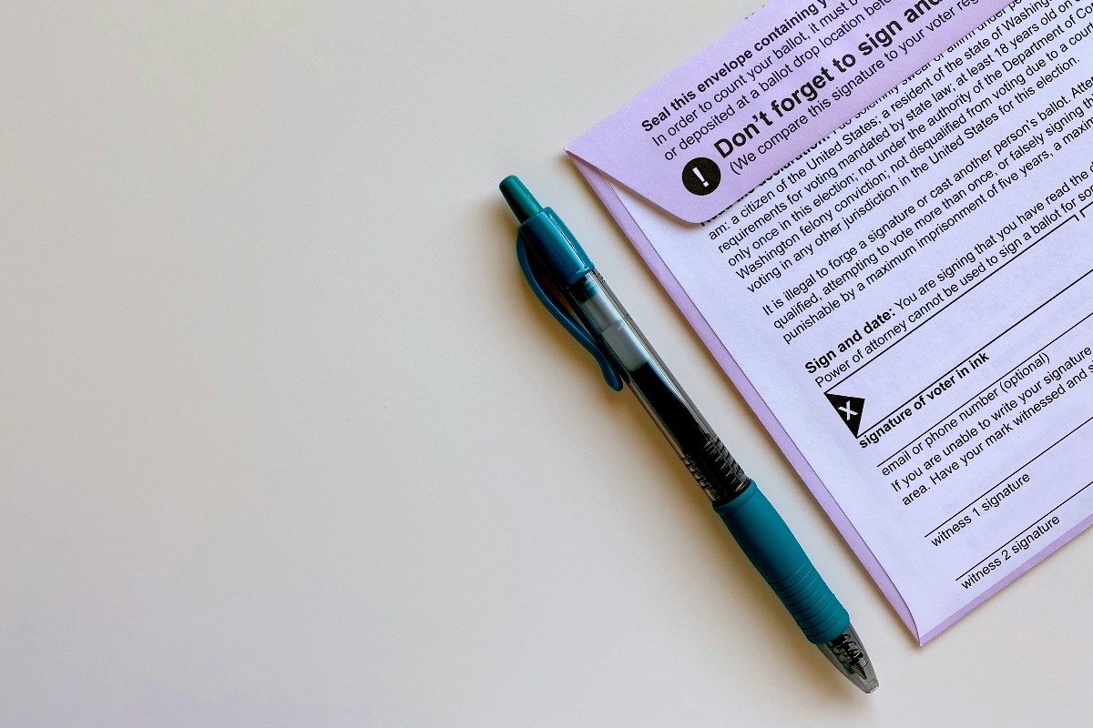 Blue and teal pen beside a purple voting ballot on a white surface.