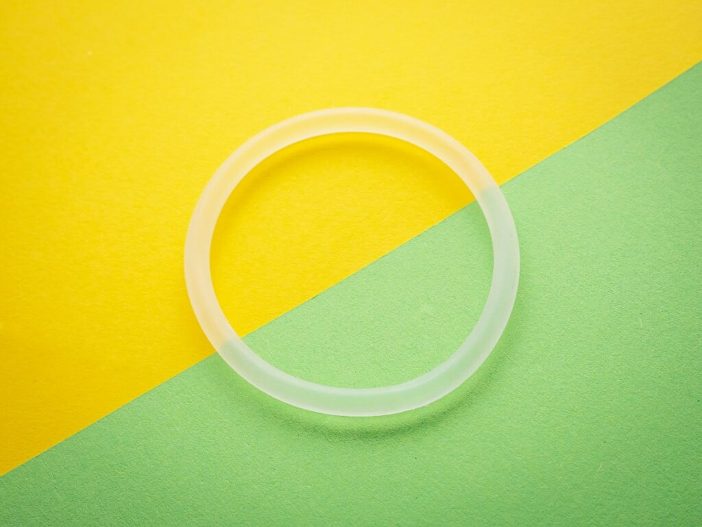 birth-control-7 - junglecity.com Clear silicone ring resting on a yellow and green diagonal backdrop on a colorful surface.