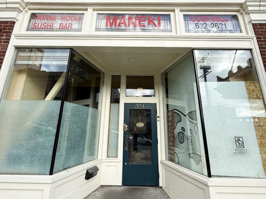 maneki-1 - junglecity.com Shopfront for a sushi bar named Maneki, with red 'MANEKI' sign above the entrance and large display windows.