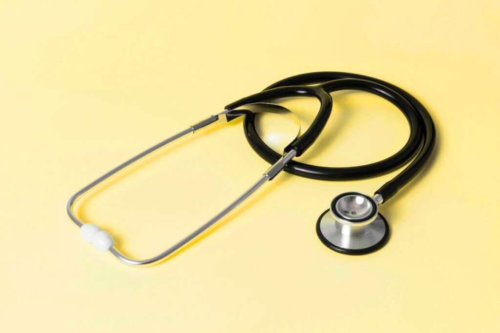 Stethoscope with black tubing and silver chest piece on a pale yellow background.