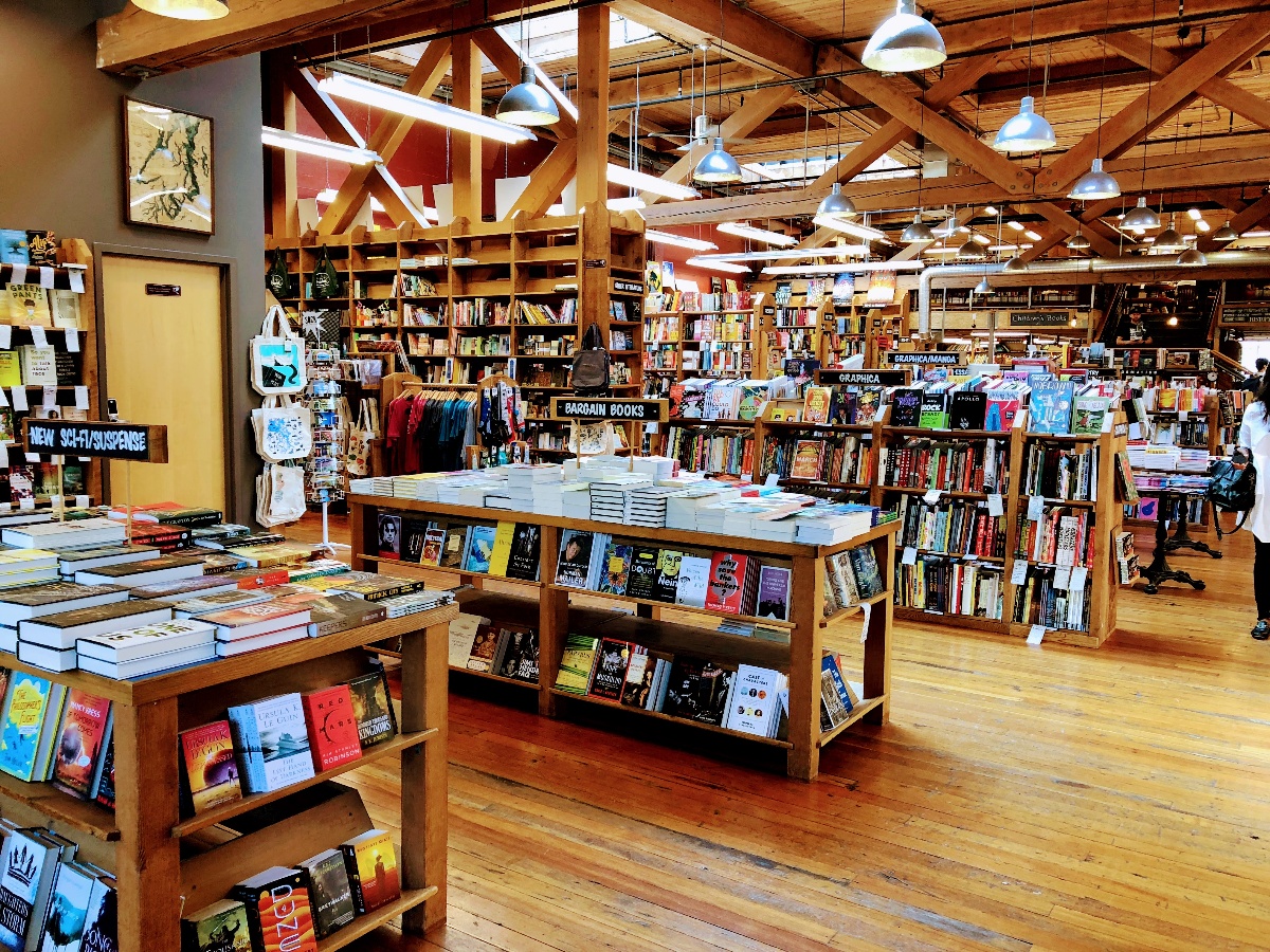 Bright wooden bookstore interior with tables of books and tall shelves under exposed beams.