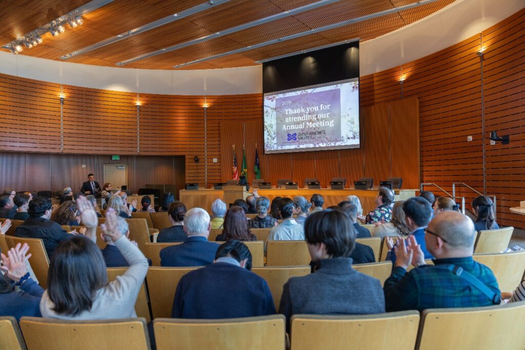 Audience in a conference room facing a stage with a large screen that reads 'Thank you for attending our Annual Meeting'