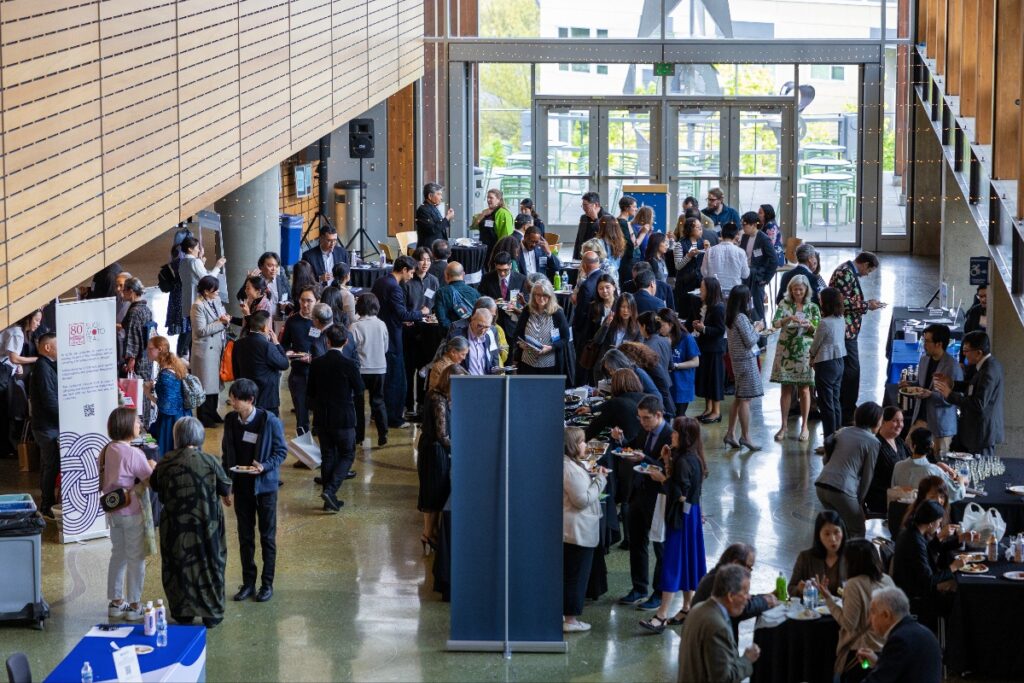 Large indoor networking event with dozens of professionals chatting near buffet tables in a modern atrium.