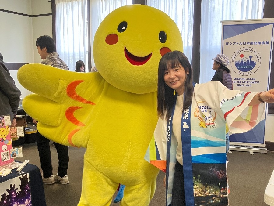 Smiling woman posing with a large yellow mascot at an indoor event.