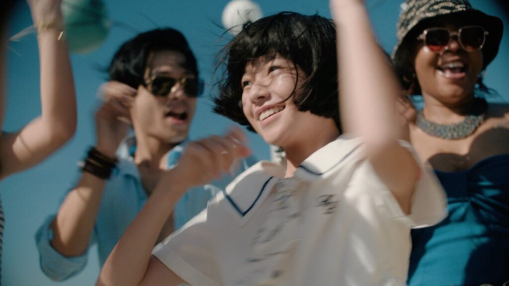 Group of friends dancing and smiling outdoors on a sunny day by the beach or park gathered together for a celebration.