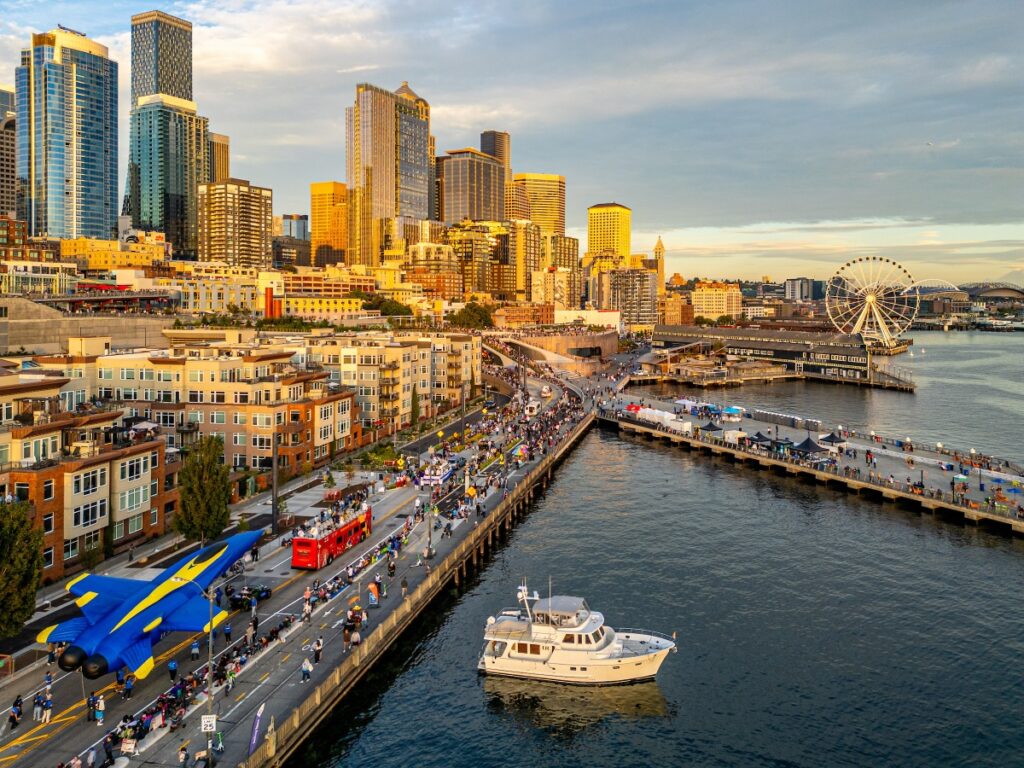 Aerial view of Seattle waterfront with tall skyscrapers, a ferris wheel, and boats in the harbor.