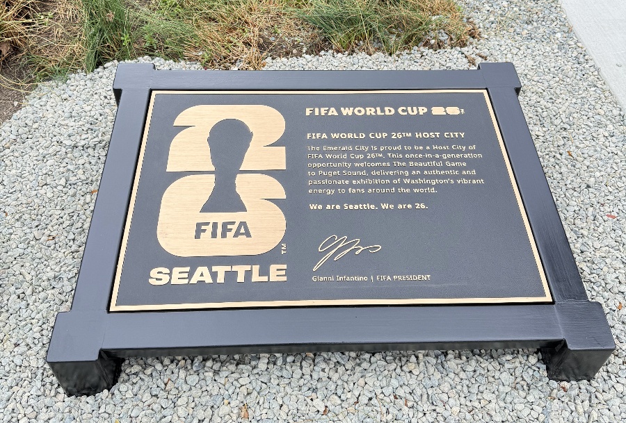 Bronze commemorative plaque on a raised frame set in a gravel area, announcing FIFA World Cup Seattle with a large logo and text.