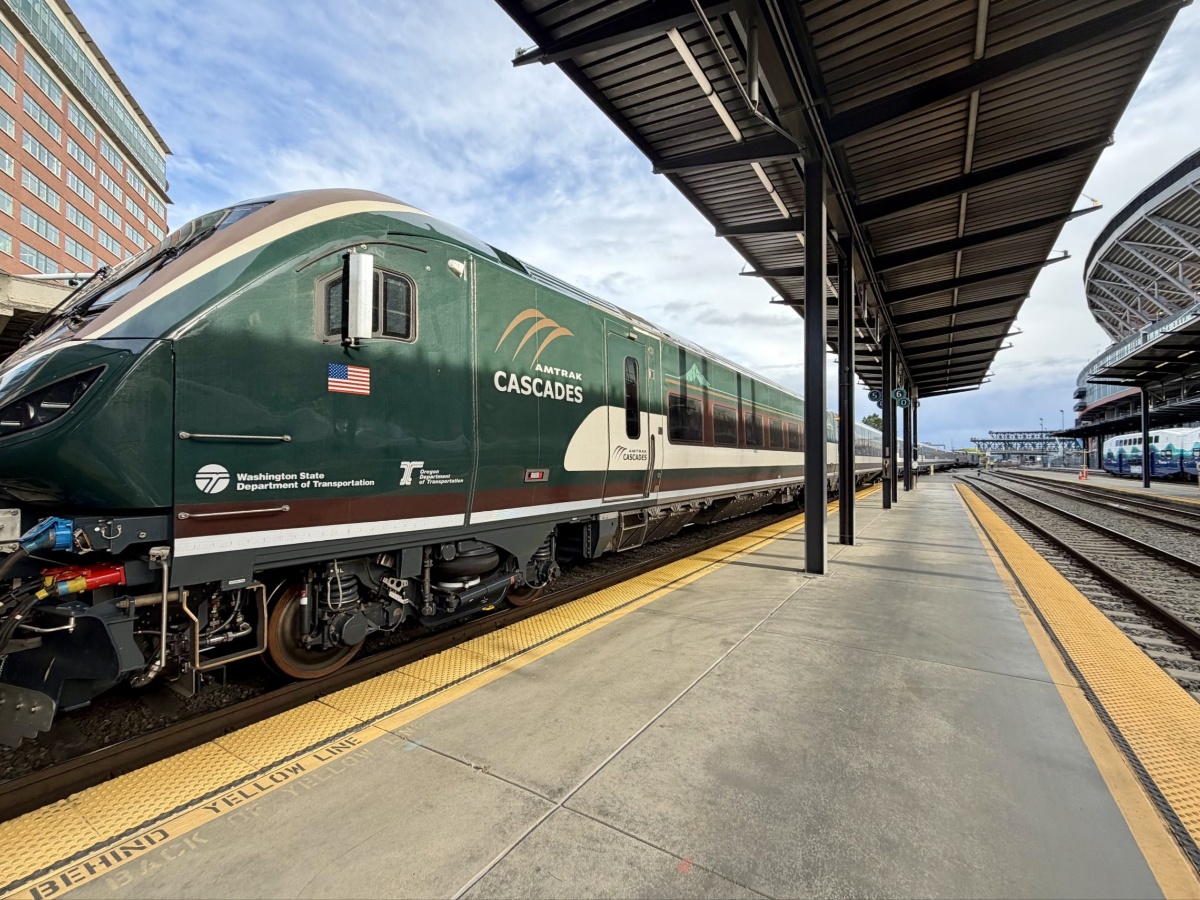 Green Amtrak Cascades passenger train at a platform with yellow tactile edge and modern station canopies above.