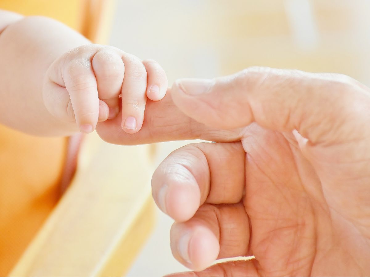 Baby's tiny finger grasping an adult's finger in a gentle handshake.