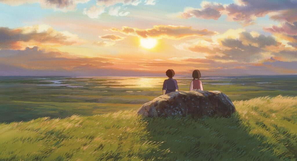 Two people sit on a rock overlooking a sunset-lit coastline from a grassy hilltop, calm sea in the distance.