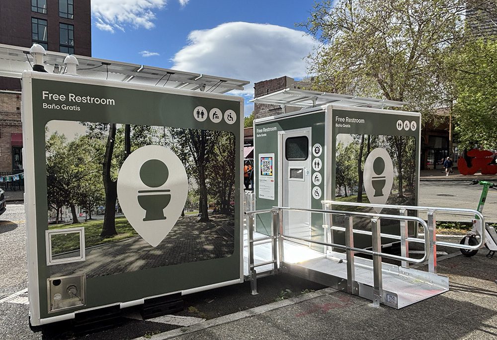 free-restrooms-2 - junglecity.com Outdoor public restroom pavilion with two green-walled kiosks and a ramp, labeled 'Free Restroom' (Baño Gratis).