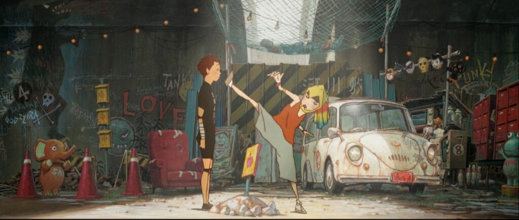 Two kids in a graffiti-covered junkyard; one girl kicks the other in a dynamic martial-arts pose next to a dusty vintage car and scattered props.