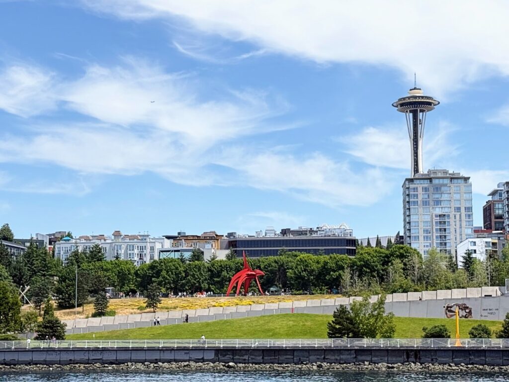 Seattle waterfront park with a red abstract sculpture and the Space Needle in the distance under a blue sky.