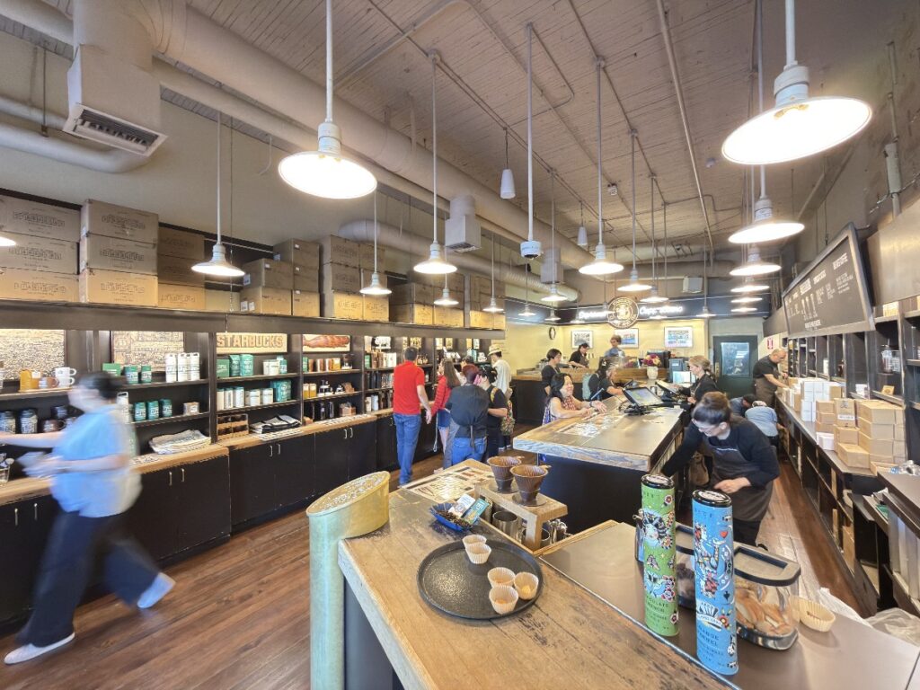 first-starbucks-17 - junglecity.com Interior of a busy coffee shop with a long service counter, baristas, and customers waiting to order or pay.