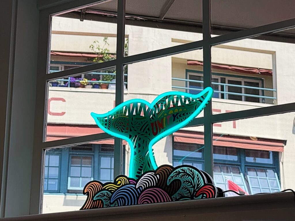 sea-beacon-1 - junglecity.com Turquoise whale-tail sculpture with intricate cutout patterns rising above a pile of colorful wave shapes seen through a window
