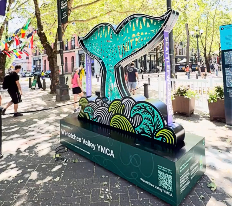 sea-beacon-6 - junglecity.com Colorful whale-tail sculpture on a pedestal promoting Wenatchee Valley YMCA in a sunny urban plaza.