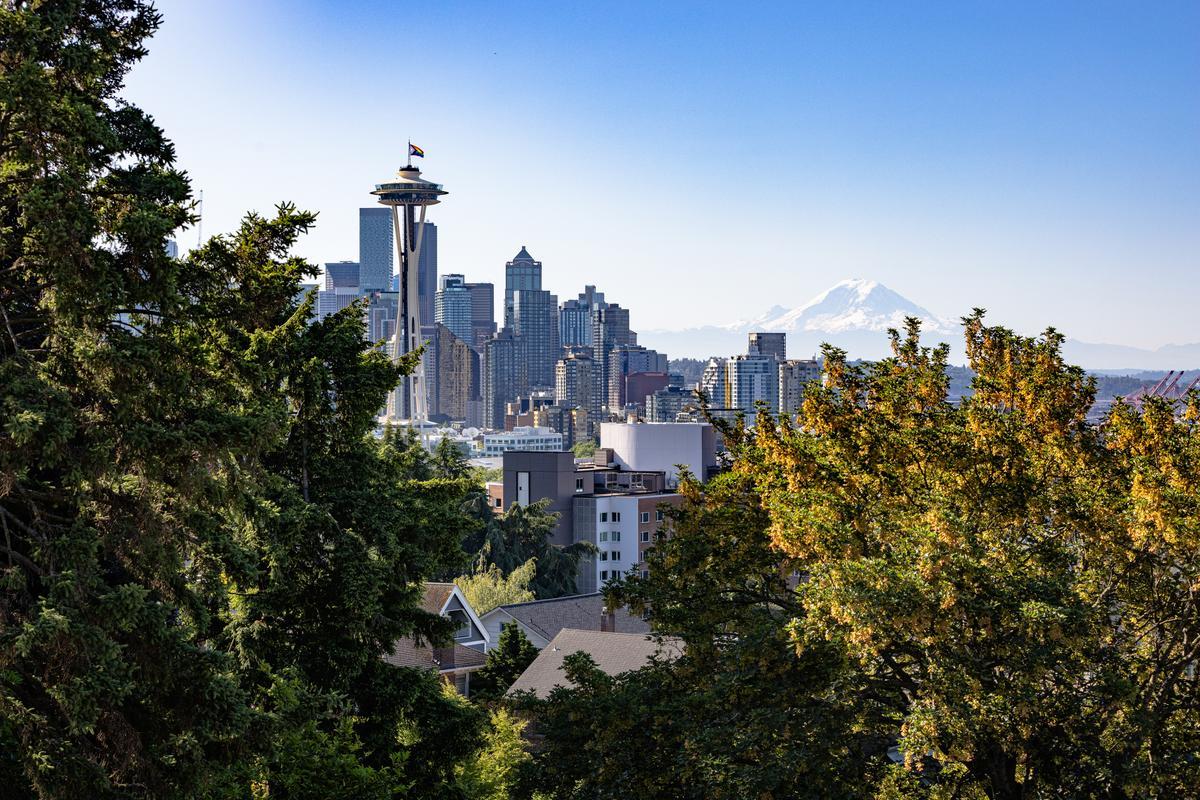 Seattle skyline with the Space Needle, seen through trees, and Mount Rainier in the distance under a clear blue sky