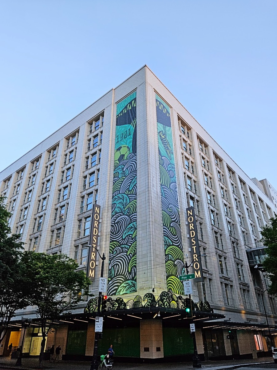 Nordstrom department store facade with a tall central mural in turquoise and blue hues against a blue sky at street level corner. **(Storefront with colorful mural)**