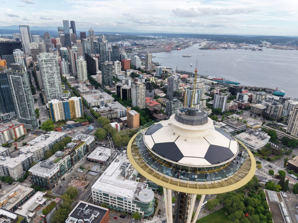 space-needle-fifa-2026 - junglecity.com Aerial view of Seattle with the Space Needle in the foreground and the downtown skyline across the bay