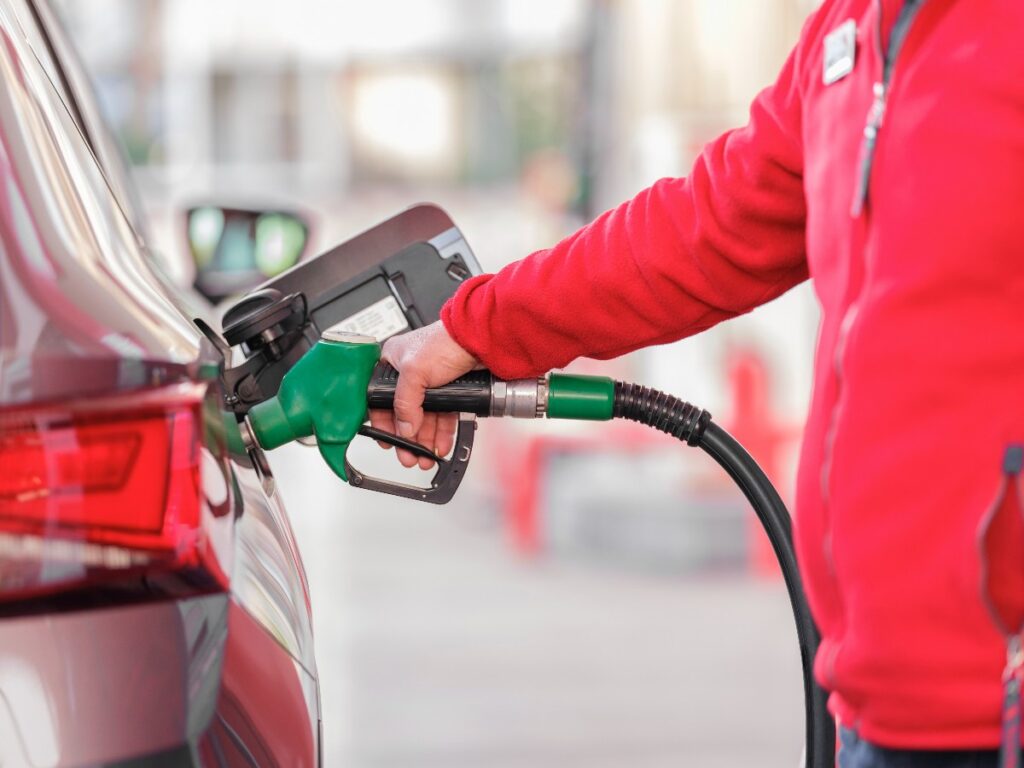Person in a red jacket refueling a car with a green gas pump nozzle at a gas station
