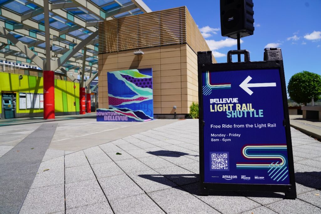 Sign advertising the Bellevue Light Rail Shuttle with a left arrow; free ride Mon–Fri 8am–6pm in bold white text on blue background.