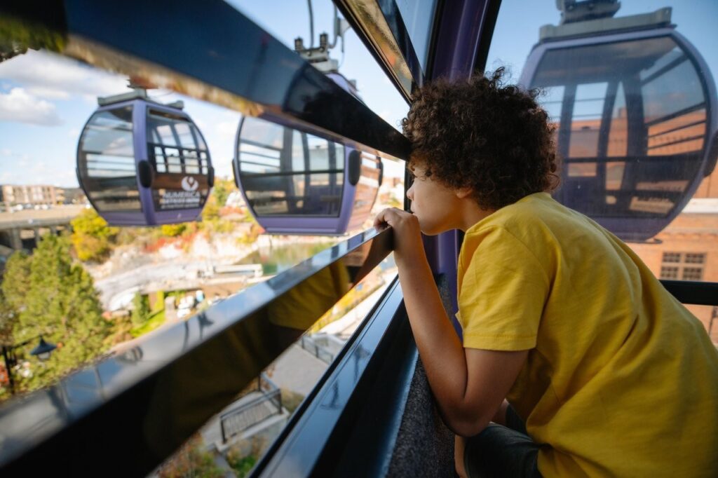 spokane-21 - junglecity.com A young child in a yellow shirt leans on a cable car window, gazing at the city below.