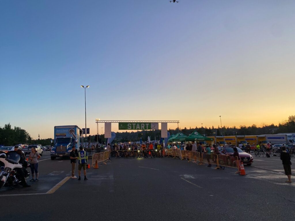 stp-3 - junglecity.com - junglecity.com Crowd of cyclists lined up at the starting gate at sunset, with volunteers and support vehicles nearby.