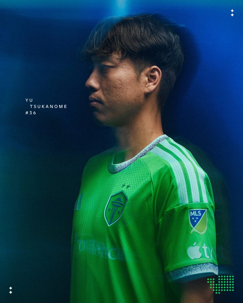 yu-tsukanome-2 - junglecity.com Portrait of Yu Tsukanome in a bright green soccer jersey against a blue gradient background, side profile view, MLS patch on sleeve.