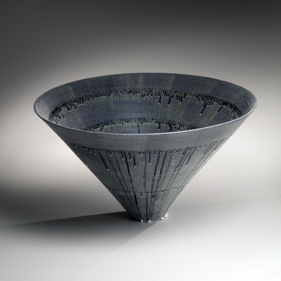 Dark gray conical funnel-shaped object with vertical ridges on a reflective surface.