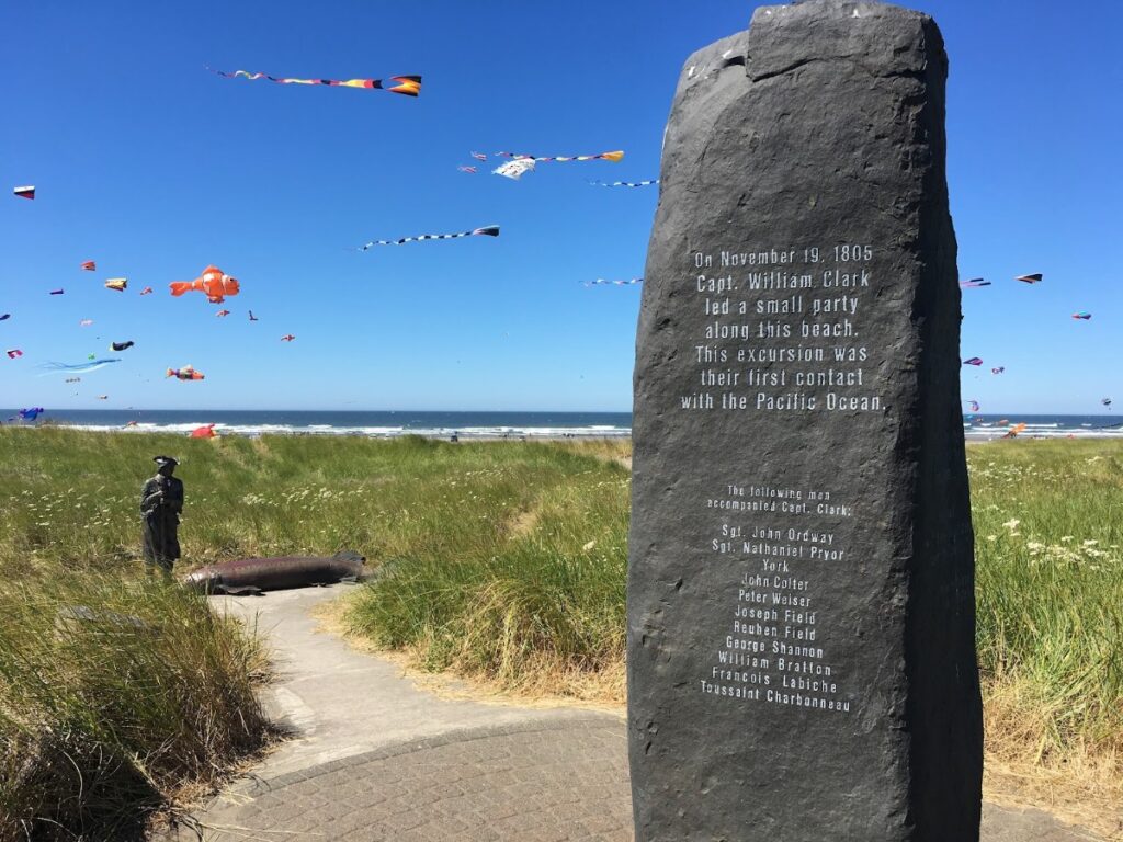 long-beach-2 - junglecity.com Granite memorial on a grassy beach with bright kites in a blue sky; engraved text honors Capt. William Clark's 1805 expedition.