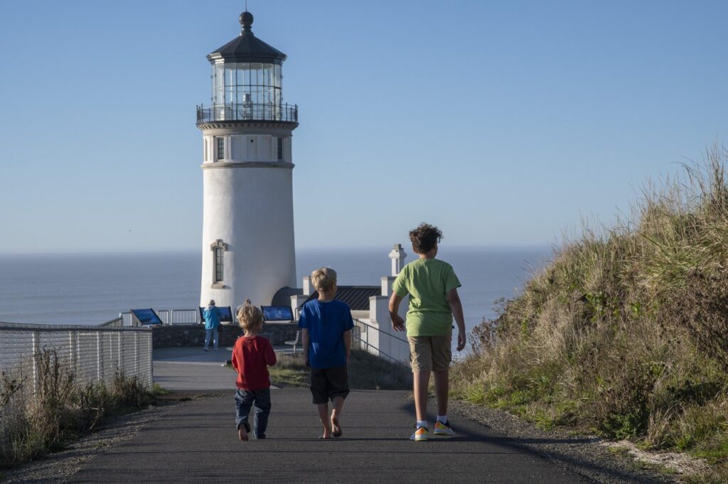 long-beach-4 - junglecity.com Three children walk toward a white lighthouse by the sea on a sunny day.