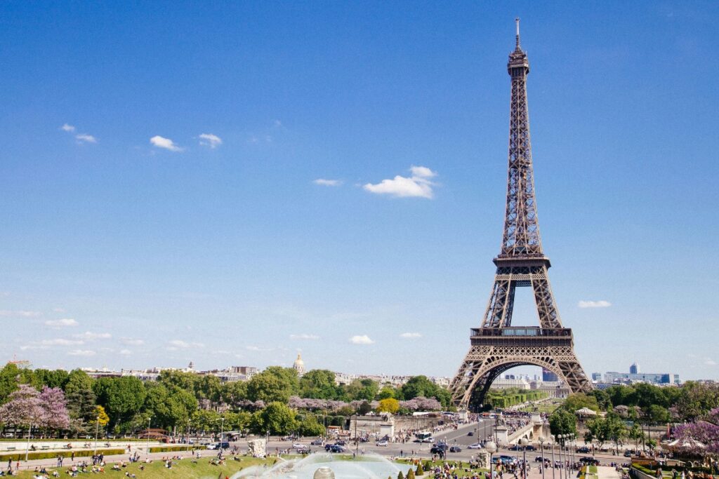 Eiffel Tower towering over the Champ de Mars with a clear blue sky and people picnicking and strolling in the foreground gardens.