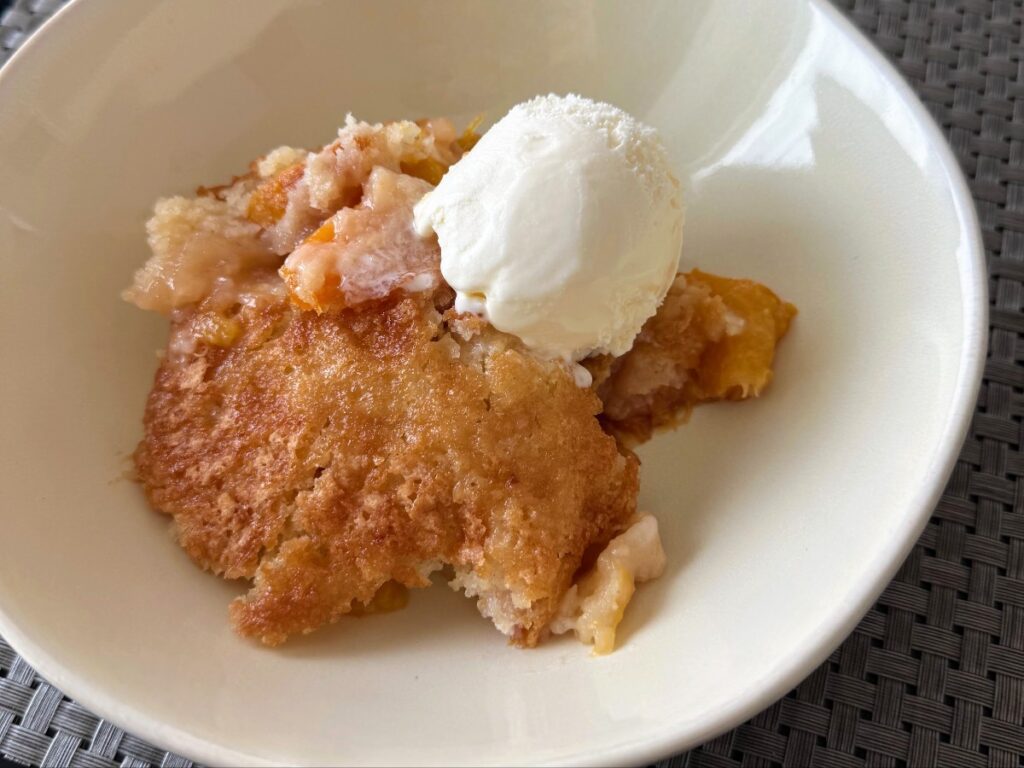 Peach cobbler with a scoop of vanilla ice cream in a white bowl.